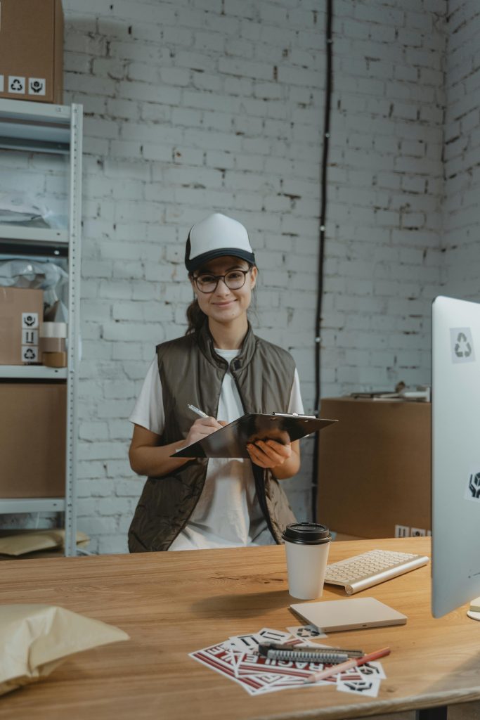 Smiling woman holding clipboard in office, managing logistics with eco-friendly focus.